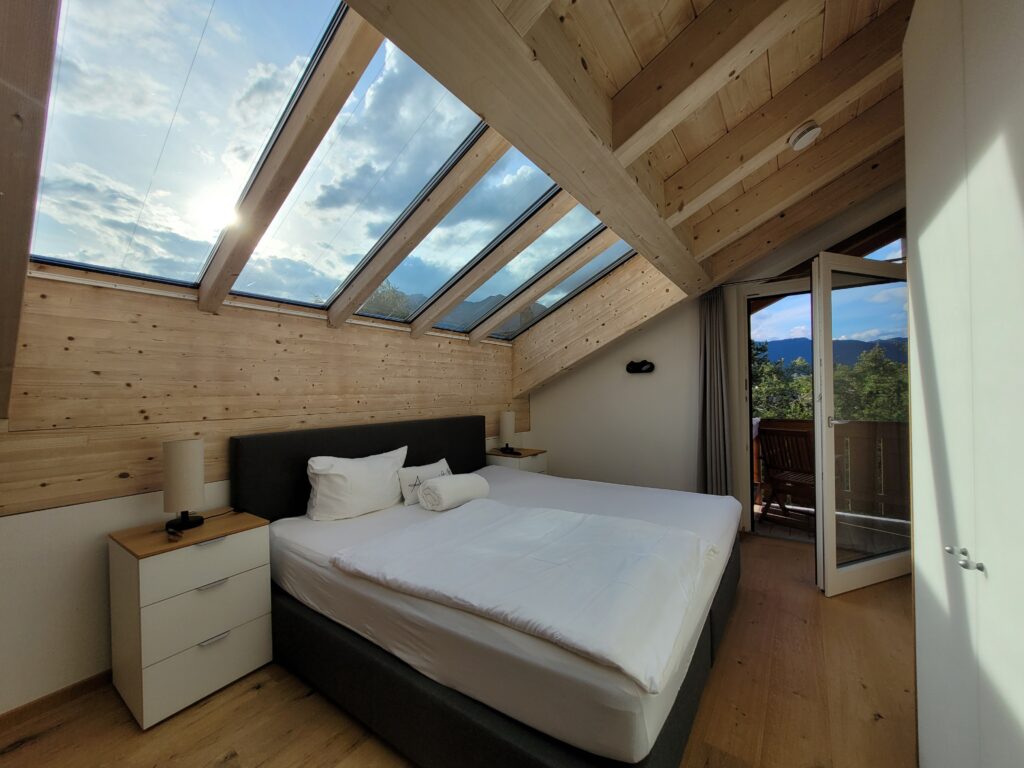 Symbolfoto "Energetische Hausreinigung". Es zeigt ein Schlafzimmer mit Dachschräge. Durch die Fenster in der Schräge fällt Sonnenschein ins Zimmer.