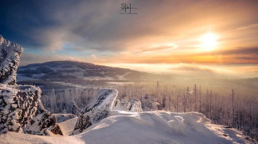 Bild vom Harz. Verschneite Winterlandschaft mit Hügeln, Wald und Sonne. Fotograf Steffen Henze.