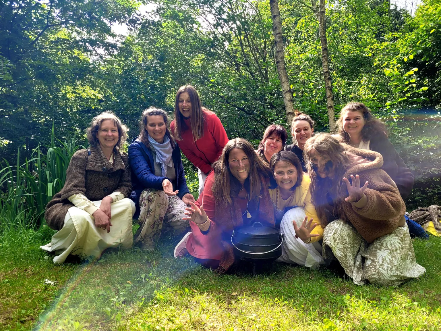 Gruppe von lächelnden Frauen, die auf einer grünen Wiese vor Bäumen sitzen. Satyadevi und Yogita sitzen in der Mitte.